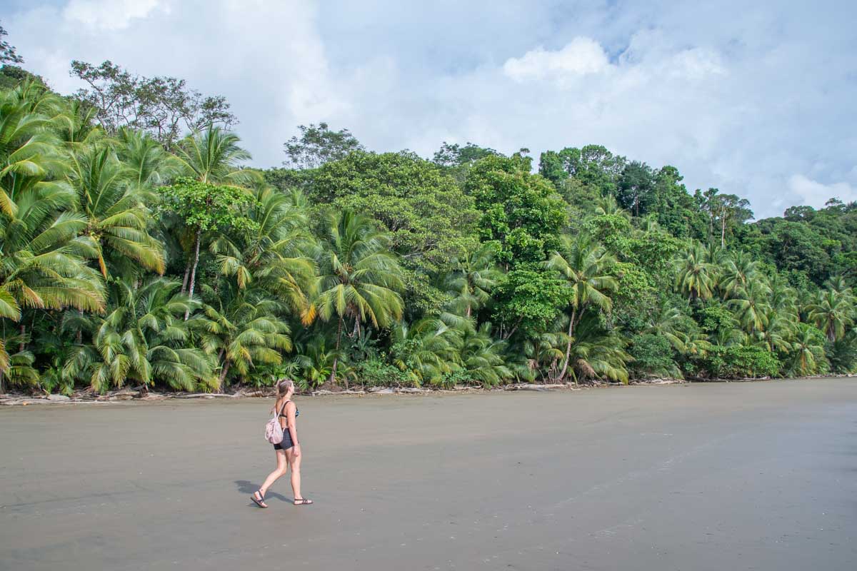 A lady walks along Arco Beach, Uvita with beautiful rainforest in the background