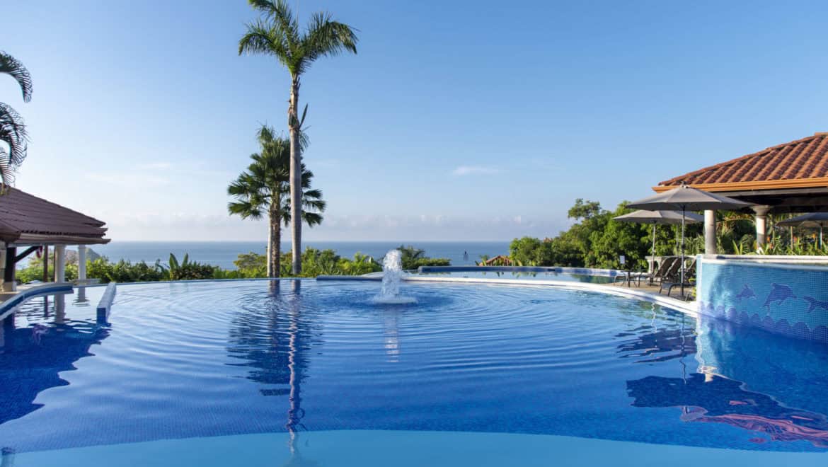 the infinity pool at Parador Resort and Spa with an ocean view and palm trees. Bright blue skies.