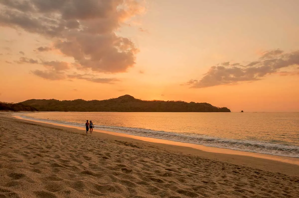 Two people walk along Playa Conchal at sunset in Costa Rica