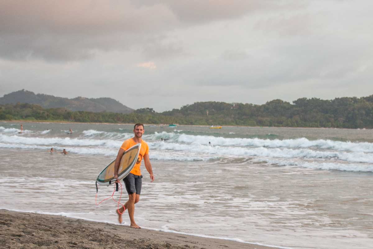 Daniel walks along Samara Beach with his surfboard