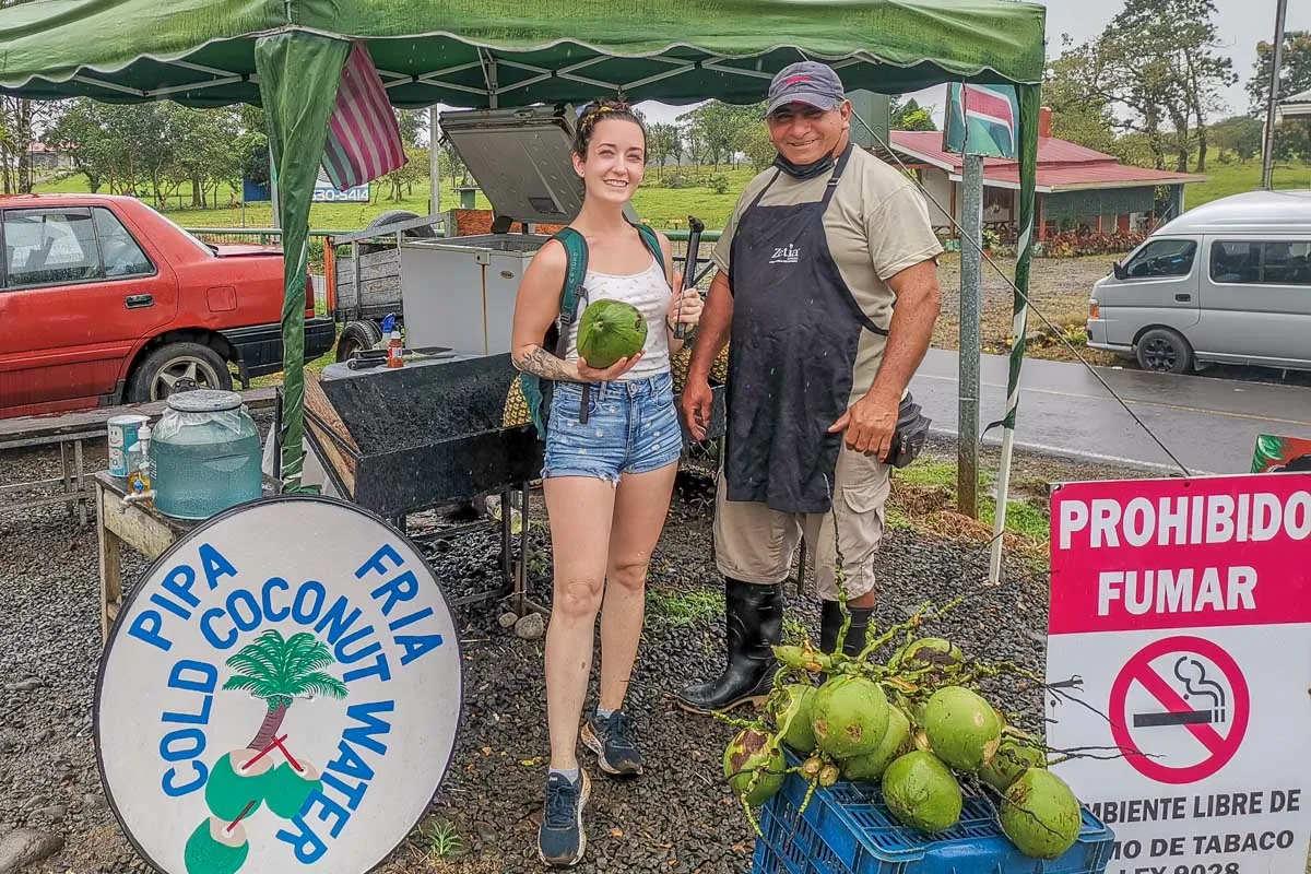 A lady takes a photo with a friendly coconut seller at Rio Celeste