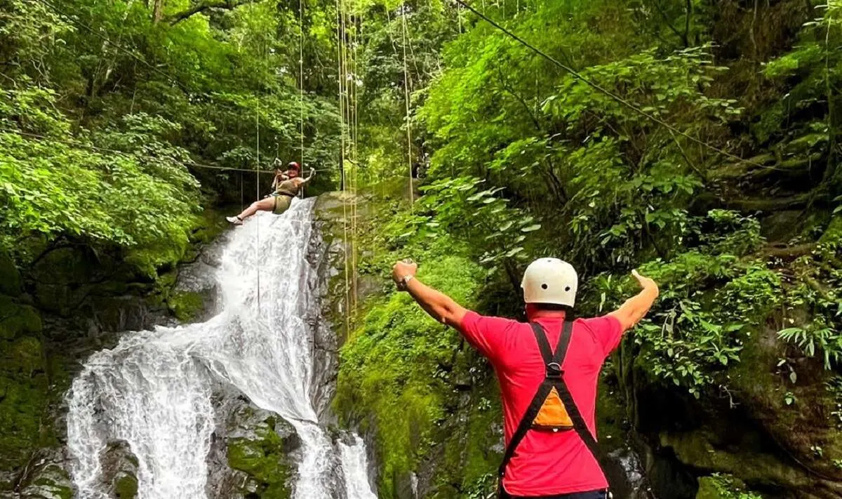 man watches a woman zipline near a waterfall in Costa Rica