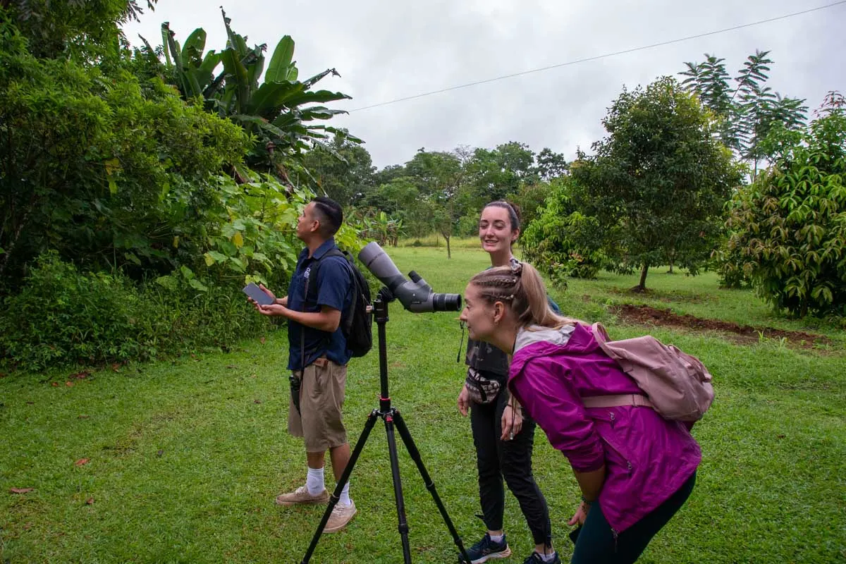 Bailey looks through a scope to search for a sloth with a guide