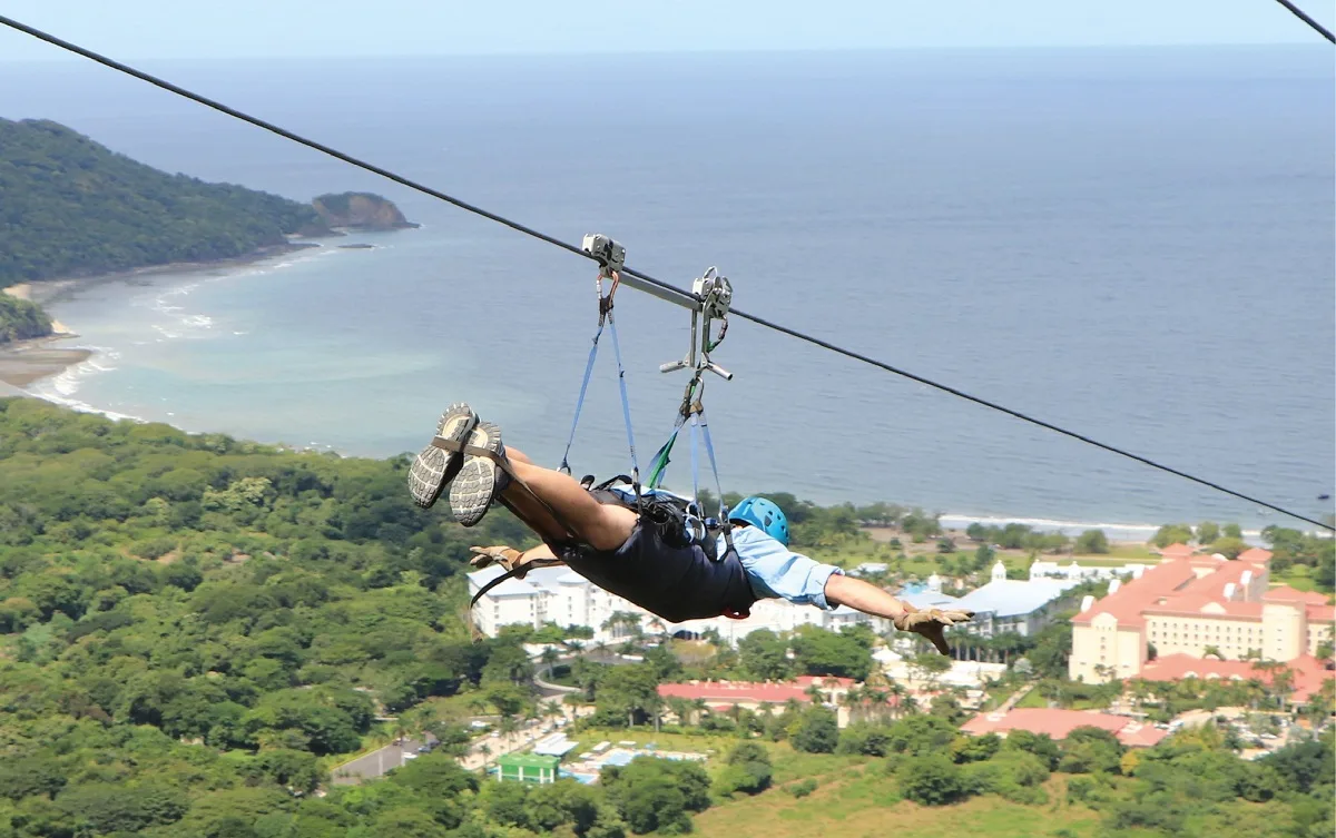 man in a superhero position going down a zipline towards the ocean
