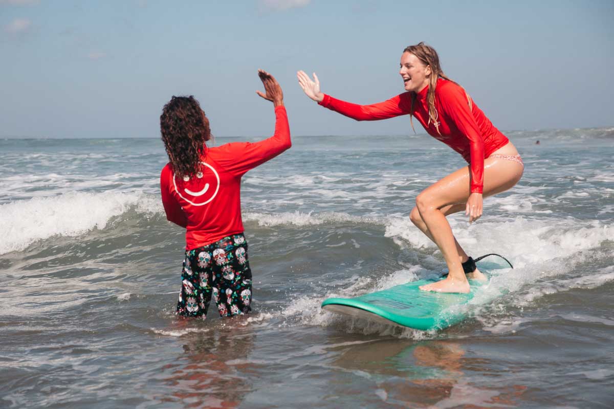 A surf instructor high fives a lady learning to surf in Tamarindo, Costa Rica