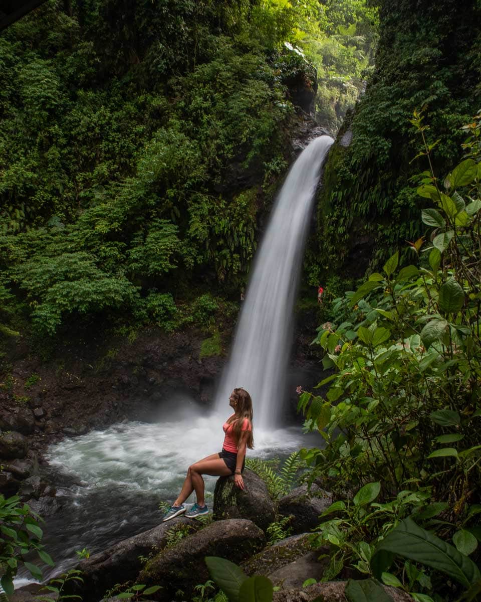 Bailey-sits-at-a-freee-waterfall-just-outside-the-La-Paz-Waterfall-Gardens seen on a tour from San Jose Costa Rica